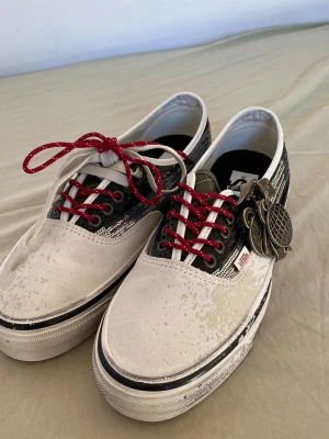 Vans  sneakers - Unika Vans sneakers i lågt snitt med vit och svart canvas, röda skosnören och coola detaljer som en ananas-nyckelring. Klassisk Vans-logga på sidan och slitstark gummisula. Perfekta för dig som gillar streetstyle och vill sticka ut.