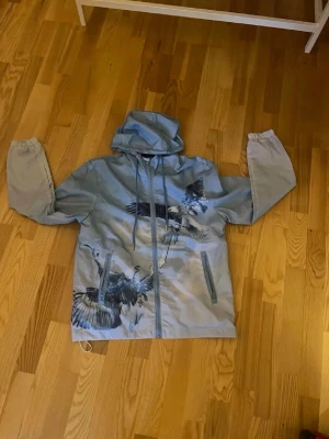 Ljusgrå vindjacka med fågeltryck - Snygg trapstar windbreaker i ljusblå med de ikoniska stora ”TRAPSTAR” på ryggen som får dig se ikonisk ut😁vid frågor bara att höra av sig jackan är inprincip i topp skick använt få gånger🔝🔝