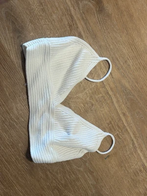 Vit ribbad kort topp med smala band - Säljer en enkel och stilren vit kort topp med ribbad struktur och smala axelband. Toppen har en mjuk och stretchig passform som gör den superbekväm. Perfekt att bära under en skjorta eller som den är till ett par höga jeans.