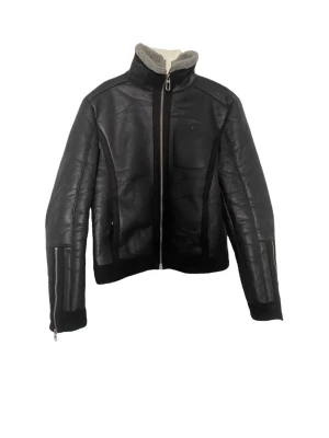 Svart skinnjacka från Armani med hög krage - Snygg svart skinnjacka med hög krage och mjukt foder. Jackan har dragkedja framtill, en bröstficka och detaljer vid ärmsluten. Perfekt för dig som vill ha en stilren och cool look.