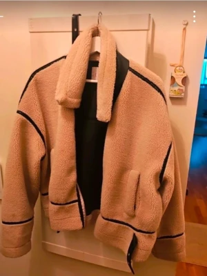 Beige teddyjacka från LOCH - Säljer en beige teddyjacka från LOCH med svarta detaljer och dragkedja. Jackan har stor krage, två fickor och är fodrad med svart material på insidan. Perfekt för kalla dagar och ger en riktigt cozy vibe.