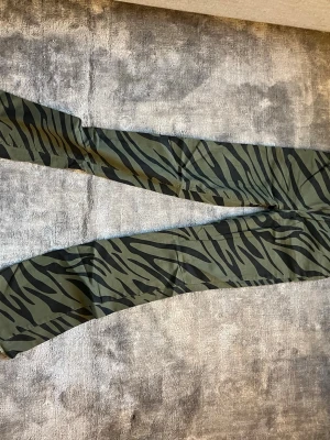 Gröna  jeans med zebramönster - Säljer ett par gröna jeans med svart zebramönster. Byxorna har bootcut ben och flera fickor, vilket ger en cool och trendig look. Låga/normala i midjan