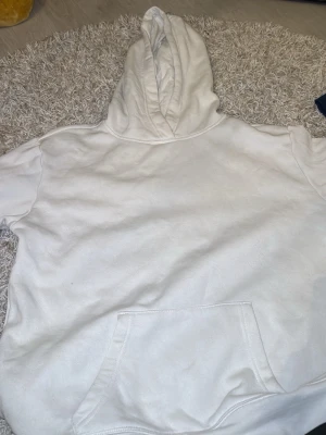 Vit hoodie med magficka - Klassisk vit hoodie med stor huva och rymlig magficka framtill. Hoodien har långa ärmar och är tillverkad i mjukt bomullsliknande material. Perfekt för en avslappnad och stilren look.