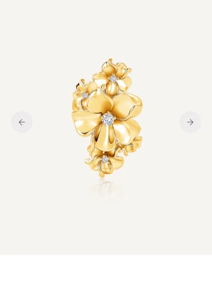 Blommig guldring med stenar - Unik ring i guldfärgad metall med stora blommor i 3D-design. Varje blomma har en liten gnistrande sten i mitten som ger extra lyxig känsla. Perfekt statement-piece för dig som vill sticka ut med din stil.