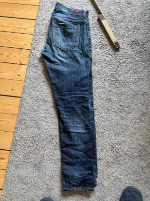 Blå jeans från dondup, George  - Säljer ett par klassiska blå jeans från dondup med snygg tvätt och kontrastsömmar. Modellen har fem fickor och detaljerade sömmar på bakfickorna. Tillverkade i slitstark denim av bomull. Perfekta för en avslappnad och trendig stil. Modellen är George och byxorna är 104 cm långa och 43 cm breda i midjan. Byxan är i storlek 34 säljer pga dem är för små