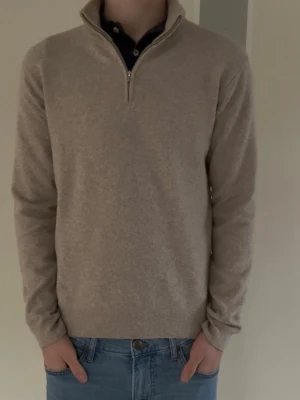 Beige halvzip tröja i ullmix - Snygg beige tröja med halvzip och hög krage, perfekt för lager-på-lager. Tröjan är tillverkad i mjuk ullmix och har ribbade muddar vid ärmslut och nederkant. Passar dig som gillar stilrena och klassiska plagg.