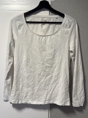 Vit långärmad topp i bomull - En basic vit långärmad topp från 157 med rund halsringning. Tillverkad i mjuk bomull, perfekt för lager på lager eller som enkel vardagsstil. Enkel och stilren design utan mönster eller detaljer.