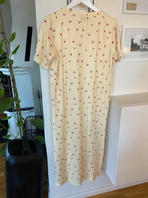 Sommarklänning! Ny med prislapp!  - Denna Liberté-klänning i modellen ALMA (9562) är en gul, långärmad klänning med körsbärsmönster, tillverkad av en mjuk blandning av polyester och elastan. Slits nedtil som är cirka 16 cm.  Klänningens totala längd 119 cm.  Dubbelstorlek S/M    