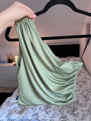 Ljusgrön oneshoulder topp (ny) - Ljusgrön oneshoulder topp från H&M i ett mjukt och följsamt material. Toppen har en draperad design och har dubbelt tyg. Perfekt för en stilren look 💚 Använd 1 gång.