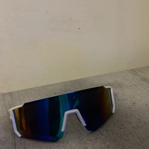 Sportiga vita solglasögon - Säljer ett par sportiga solglasögon med vit båge och stora spegelblå linser. Glasögonen har en futuristisk, kantig form och passar perfekt för dig som gillar en modern och cool stil.