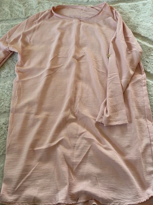 Ljusrosa långärmad klänning - En enkel och stilren ljusrosa klänning med lång ärm och rund halsringning. Klänningen är rak i modellen och tillverkad i ett mjukt bomullsliknande material. Perfekt för en avslappnad look.