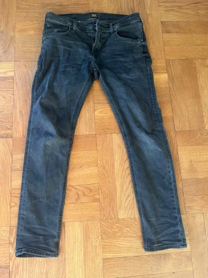 Svarta slim fit/straight leg jeans från Lee - Säljer ett par svarta jeans från Lee med klassisk femficksmodell, storlek 30/30. Jeansen är i slim fit/straight leg modell. Perfekt mix. De har en snygg tvättad look och är tillverkade i stretchigt denimtyg för extra komfort. Inga defekter