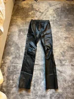 Svarta byxor i skinnimitation  - Snygga svarta byxor i skinnimitation från Kaffe. De har en elastisk midja och raka/utsvängda ben, vilket ger en cool och modern look. Perfekta för dig som vill ha ett statement-plagg i garderoben.