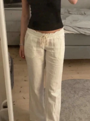 Vita linnebyxor med dragsko - Säljer ett par vita linnebyxor med avslappnad passform och dragsko i midjan. Byxorna har raka ben och sidofickor, perfekta för en chill och stilren look. Tillverkade i lätt och luftigt linnematerial.