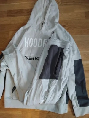 Grå HOODRICH loungewear set - Snyggt loungewear set från HOODRICH i ljusgrått med mörkgrå detaljer. Setet består av en hoodie med tryck framtill och matchande byxor med dragkedjeficka och dena  har ett litet hål på hoodien och byxorna är L o hoodien är M