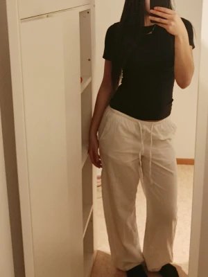 Beiga linnebyxor med dragsko - Säljer ett par beiga linnebyxor med avslappnad passform och dragsko i midjan. Byxorna har raka ben och sidofickor, perfekta för en chill och stilren look. Materialet är linne vilket gör dem luftiga och bekväma.