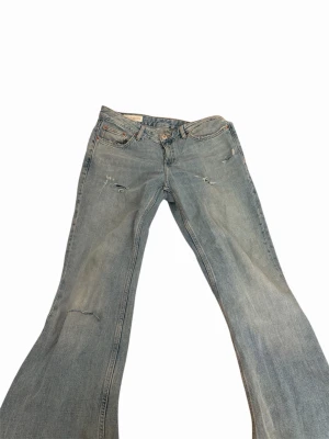 Ljusblå bootcut jeans med slitningar - Säljer ett par ljusblå bootcut jeans med slitna detaljer och lätt tvättad look. Jeansen har klassisk femficksmodell, låg midja och vida ben. Perfekta för dig som gillar retrostil och vill ha ett par riktigt snygga jeans🩷