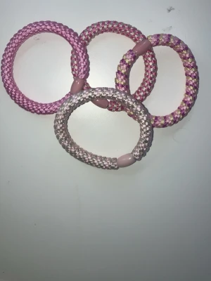 Fyra rosa hårsnoddar i tyg - Fyra tjocka hårsnoddar i olika nyanser av rosa och lila med flätad design och plastdetalj. Perfekta för att sätta upp håret med en färgglad touch. Säljs som ett set.