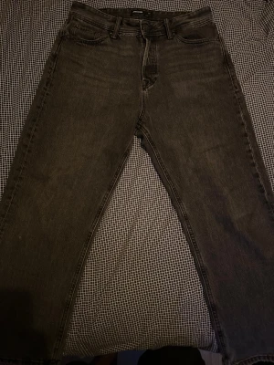Svarta raka jeans från Jack & Jones - Säljer ett par svarta jeans från Jack & Jones med rak passform. Jeansen är tillverkade i bomull och har klassisk femficksdesign samt bälteshällor. Perfekta för en avslappnad och stilren look.