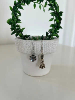 Påskötonhängen - Unika örhängen i silverfärgad metall, ena med en söt kanin och den andra med en blomma. Båda har små pärldetaljer ovanför hängen. Perfekt för dig som gillar påsk 🐣