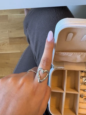 Silvrig hjärtformad ring - Säljer en snygg ring i silverfärgad metall med en öppen hjärtformad design. Ringen har en modern och trendig look som verkligen sticker ut. Perfekt accessoar för att lyfta din outfit.