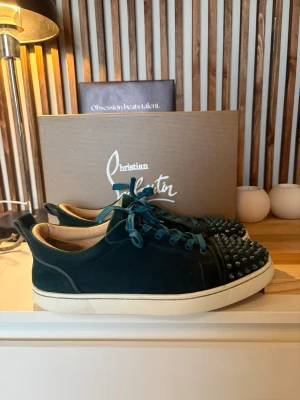 Christian Louboutin sneakers - Snygga mörkgröna sneakers från Christian Louboutin i mocka med matchande gröna skosnören och vita sulor. Tåpartiet är dekorerat med coola nitar som ger en edgy vibe. Perfekta för dig som vill sticka ut med exklusiva detaljer och unik design.
