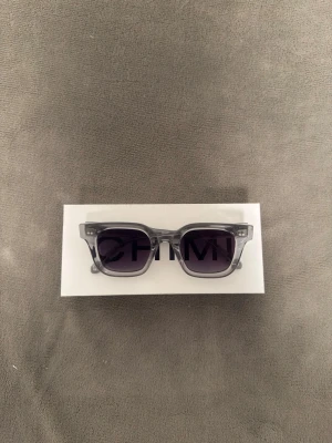  CHIMI grå solglasögon - Säljer ett par stilrena solglasögon från CHIMI med transparent grå båge och mörka, fyrkantiga linser. Snygg och modern design som passar till många looks. Perfekta för dig som vill ha en clean och trendig accessoar. PRIS KAN DISKUTERAS