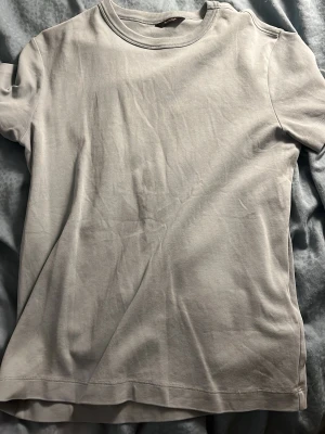 Ljusgrå basic t-shirt från Morris - En stilren ljusgrå t-shirt från Massimo dutti med klassisk rund halsringning och korta ärmar. Tillverkad i mjuk bomull som känns skön mot huden. Perfekt att matcha med jeans eller shorts för en clean look. 