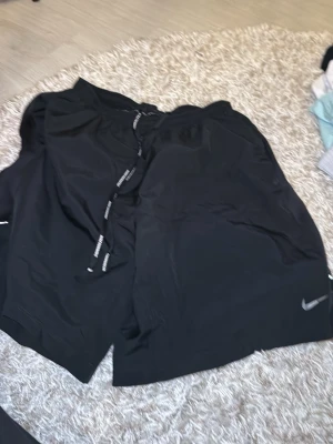 Svarta Nike shorts med snörning - Säljer ett par svarta shorts från Nike med snörning i midjan och diskret logga på benet. De har en avslappnad passform och är perfekta för träning eller chill. Materialet känns lätt och sportigt.