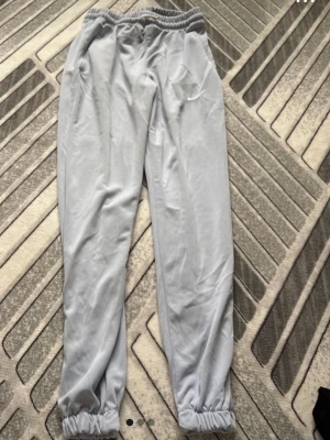 Ljusgrå mjukisbyxor  Nike - Säljer ett par ljusgrå mjukisbyxor  Nike med broderad logga på benet. Byxorna har resår i midjan och vid bensluten samt två sidofickor. Perfekta för chill dagar eller träning. Mjukt och bekvämt material.not real nike