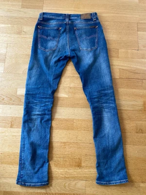 Nudie Jeans W32 L32 - Säljer ett par klassiska blå jeans från Nudie Jeans med slimfit. Jeansen har två bakfickor med den ikoniska Nudie-sömmen och läderpatch i midjan. Perfekta för dig som gillar en avslappnad men stilren look. Skriv vid frågor:)
