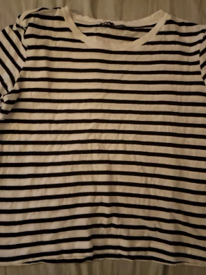Randig t-shirt från Zara - Säljer en klassisk svartvit randig t-shirt från Zara. T-shirten har korta ärmar, rund halsringning och är gjord i mjuk bomull. Perfekt för en enkel och stilren look.