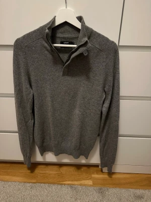 Grå Kashmir tröja från Celio - Mysig grå Kashmir tröja från Celio med hög krage och half zip-dragkedja. Tröjan har ribbade muddar vid ärmslut och nederkant samt lång ärm. Perfekt för lager på lager och enkel att matcha till olika outfits.100% Kashmir