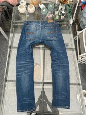 Nudie Jeans Lean Dean W33/L32 blå denim - Säljer ett par Nudie Jeans Lean Dean i storlek W33/L32. Klassiska blå slim tapered jeans med snygga slitningar och naturlig fading.  Modellen Lean Dean är en av Nudies mest populära fits – slim över låren och smalare nedåt, med lite stretch för bättre komfort.  Detaljer • Märke: Nudie Jeans • Modell: Lean Dean • Storlek: W33 / L32 • Färg: blå denim • Material: 99% bomull, 1% elastan • Skick: bra skick  Perfekta streetwear / vardagsjeans och passar till sneakers, hoodie eller t-shirt. 