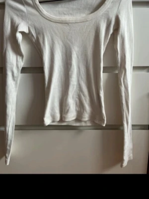 Vit långärmad topp med rund hals - En enkel och stilren vit långärmad topp med rundad halsringning. Toppen är figurnära och tillverkad i mjukt bomullsmaterial, perfekt att matcha med jeans eller kjol för en clean look.