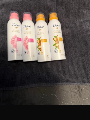 Dove Shower Mousse duschmousse 4-pack - Fyra flaskor Dove Shower Mousse i olika dofter: två med ros och två med arganolja. Flaskorna är vita med rosa eller orange detaljer och har praktiska plastlock. Perfekt för dig som vill ha en lyxig duschupplevelse med mjukgörande mousse.