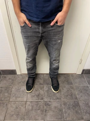 Jack&Jones Slim/Glenn - Riktigt feta grå Jack & Jones jeans med slitningar. Modell: Slim/Glenn. Mycket bra skick. A=41CM B=97,5CM C=16,5CM. Modellen är 173cm, 64kg. Pris kan diskuteras!!