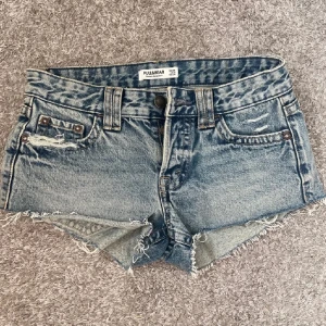 Blå jeansshorts från Pull&Bear - Snygga blå jeansshorts från Pull&Bear med råa kanter och slitna detaljer. Klassisk femficksmodell med knapp och dragkedja framtill. Perfekta för varma dagar och en avslappnad stil. Passar mig som brukar ha xs