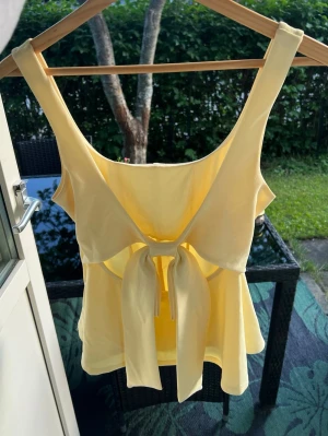 Gul linnetopp med knyt i ryggen - Säljer en söt ljusgul linnetopp från Bik Bok i storlek S 🍯Nypris 399kr, säljer för 100kr 🌸Har en liten fläck i tyget på insidan som inte syns utåt