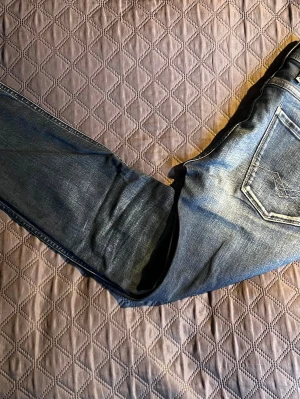 Blå slim fit jeans från Replay - Snygga blå slim fit jeans från replay med klassisk femficksdesign och diskreta slitningar framtill. Jeansen har normal midja och raka ben, tillverkade i mjuk denim med lite stretch för extra komfort.