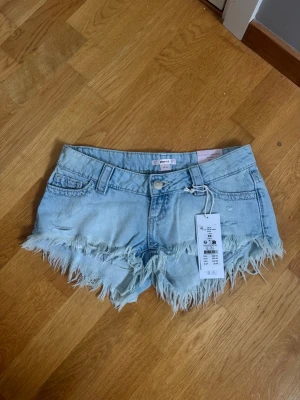 Ljusblå jeansshorts med fransig kant - Snygga lågmidjade ljusblå jeansshorts från Gina 14+. Helt nya med lappen kvar. Köpta för 300 kr. 