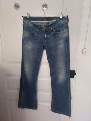 Blå lågmidjade bootcut jeans från ONLY - Säljer ett par blå bootcut jeans från ONLY med klassisk femficksdesign. Jeansen har låg midja och är tillverkade i denim med stretch för skön passform samt lite bootcut vid anklarna. De är W29 och L32