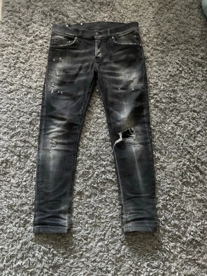 Dondup jeans - Säljer ett par svarta skinny jeans med slitningar och hål på ena benet. 39cm bredd 90cm Längd. Jeansen har en tvättad look med ljusare partier och detaljerade slitningar framtill. Pris går att diskuteras.