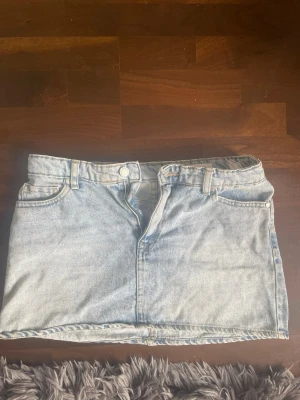 Ljusblå jeanskjol från Bershka - Trendig ljusblå jeanskjol från Bershka med klassisk femficksdesign, bälteshällor och knappstängning fram. Perfekt till sommaren och enkel att matcha med olika toppar för en cool och avslappnad look.