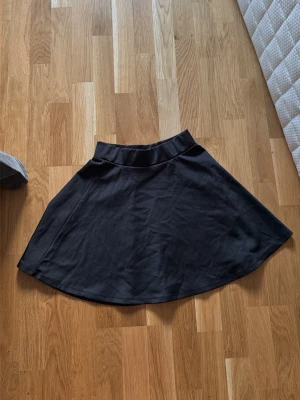 Svart vid kjol i bomull - En svart, vid kjol med hög midja och enkel design. Kjolen har en mjuk och följsam bomullskänsla och är lätt att matcha med olika toppar. Perfekt för dig som gillar en stilren och avslappnad look.