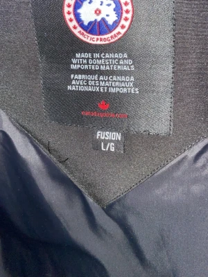 Svart dunjacka från Canada Goose - Säljer en svart dunjacka från Canada Goose i storlek L. Jackan är tillverkad i Kanada med både inhemska och importerade material. Fylld med dun och fjädrar för maximal värme under kalla vinterdagar. Klassisk design med hög krage och slitstarkt yttertyg.