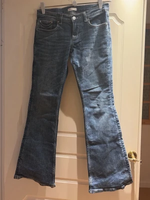 Blå bootcut jeans med broderade fickor - Snygga blå bootcut jeans med klassisk femficksdesign och broderade detaljer på bakfickorna. Jeansen har en lätt tvättad look och vida ben nedtill. Perfekta för dig som gillar retrostil och vill ha ett par jeans med lite extra attityd.