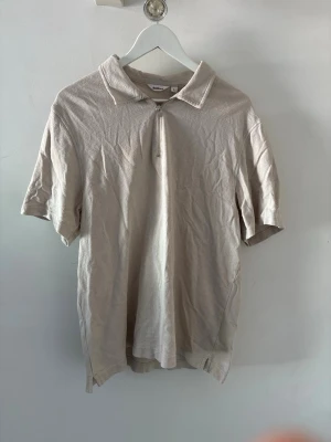 Beige piké med dragkedja Dobber Zip - Stilren beige pikétröja med kort ärm och dragkedja framtill istället för knappar. Klassisk krage och rak passform, perfekt för en avslappnad men ändå snygg look. Tillverkad i mjukt material som känns skönt mot huden.