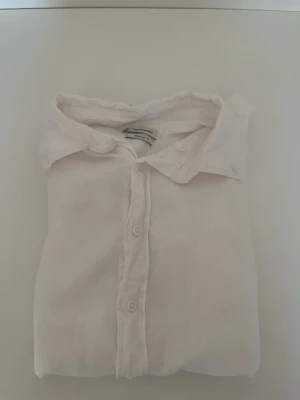 Vit klassisk skjorta i bomull - Säljer en stilren vit skjorta med klassisk krage och knappar framtill. Skjortan har lång ärm och är tillverkad i mjuk bomull, perfekt för en clean och enkel look. Passar till det mesta och är ett måste i garderoben.