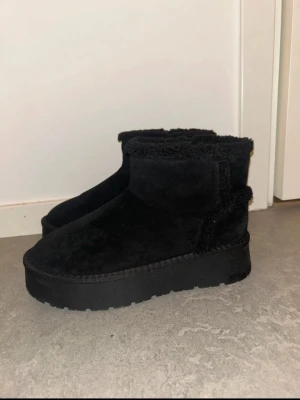 Svarta ankelhöga platåstövlar - Säljer ett par svarta stövlar med fluffig insida och utsida samt rejäl platåsula. De är ankelhöga och har en enkel, stilren design utan synliga detaljer. Perfekta för dig som vill ha både värme och stil under kalla dagar. Skorna är aldrig använda bara testade för jag har inte hittat något tillfälle för dom men dom är extremt mysiga❤️